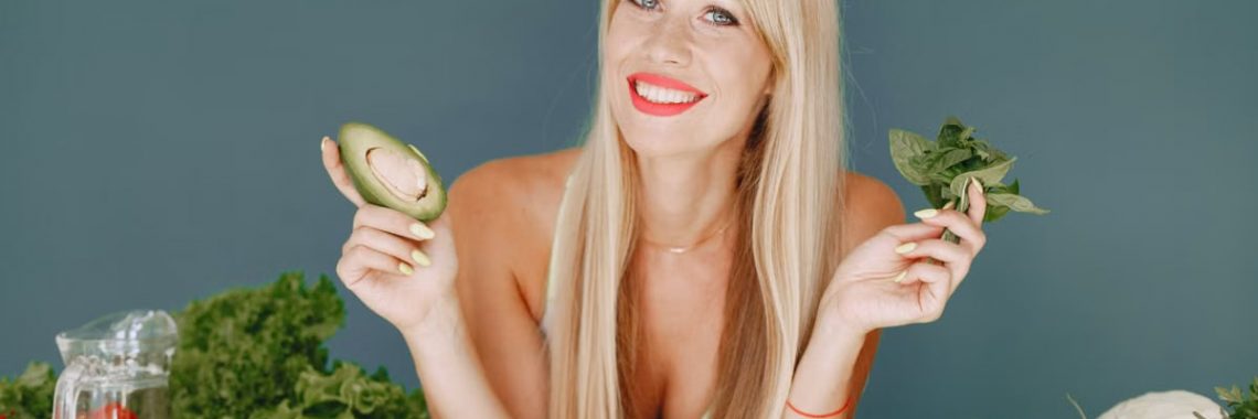 Blonde woman promotes healthy eating with fresh vegetables and fruits on display.
