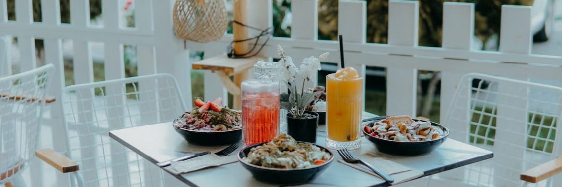 A cozy outdoor cafe table with colorful salads, refreshing drinks, and a serene garden view.