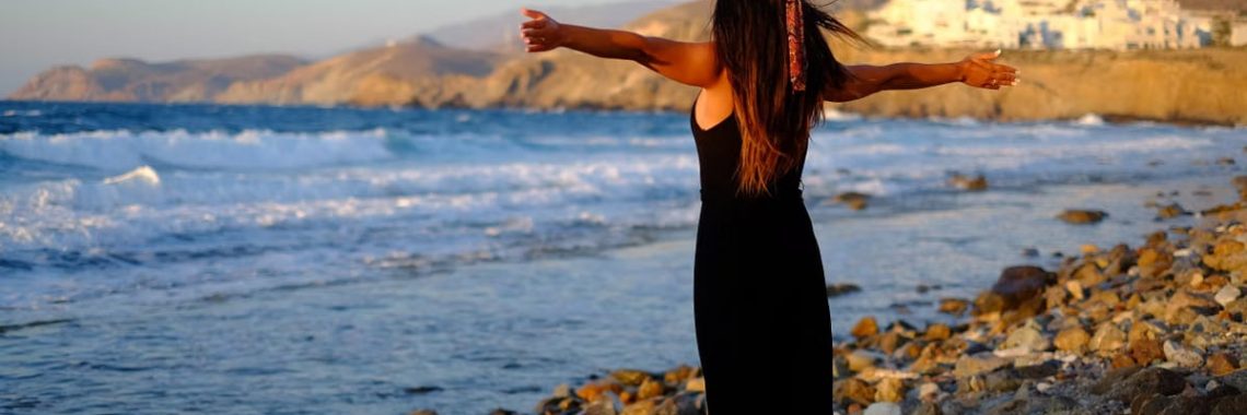 Woman enjoying freedom at sunset on a rocky beach in Greece.